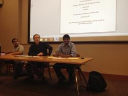 Three people sitting at a table in front of a projection screen