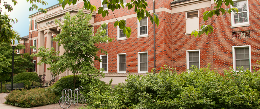 Edged with shrubbery and trees, and with a bike rack at its columned entrance, Gilbert Hall was once the campus hospital.