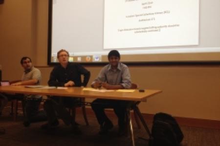 Three people sitting at a table in front of a projection screen